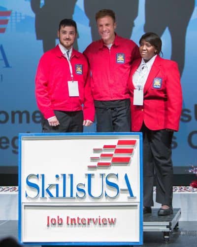 Students at SkillsUSA job interview event wearing red jackets, representing higher education and car.