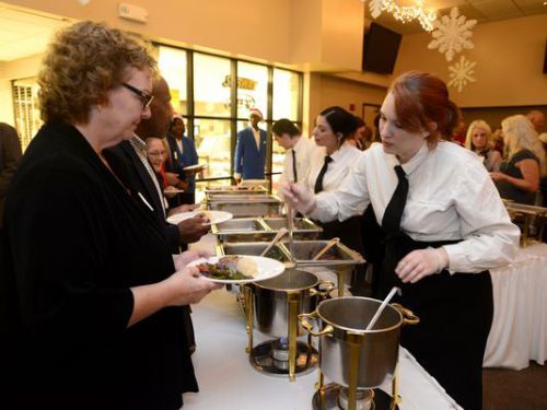 Culinary students in white uniforms serving food at a hospitality event.