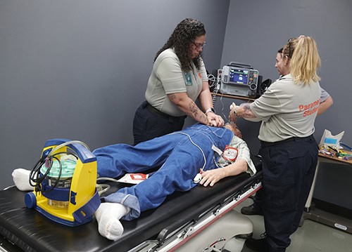 Paramedic training simulation with students practicing patient care on a medical mannequin.