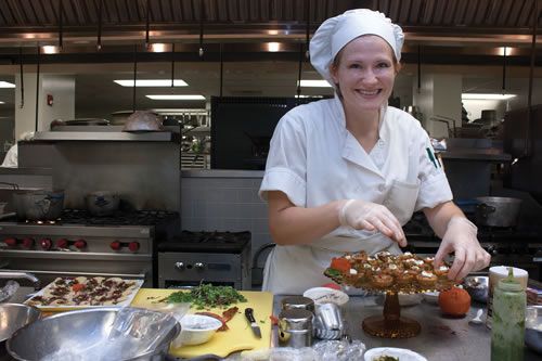 Culinary arts student in chef uniform decorating a cake in a commercial kitchen setting.
