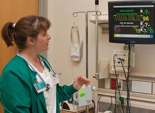 Electrocardiograph technician monitoring patient heart activity with ECG machine.