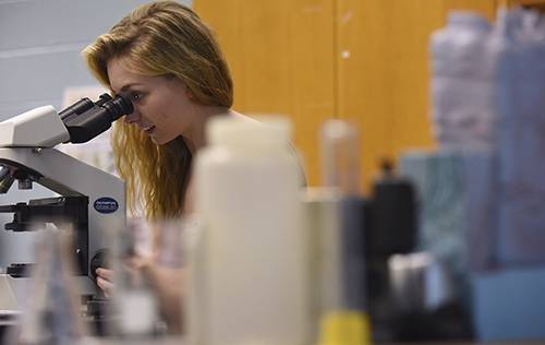 Biochemistry student using a microscope in a laboratory setting for scientific research.