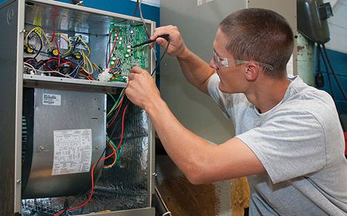 Electrical technician performing HVAC system wiring and maintenance.