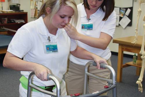 Students practicing gait training with assistive devices in a clinical setting.