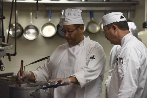 Professional culinary students preparing food in a commercial kitchen setting.