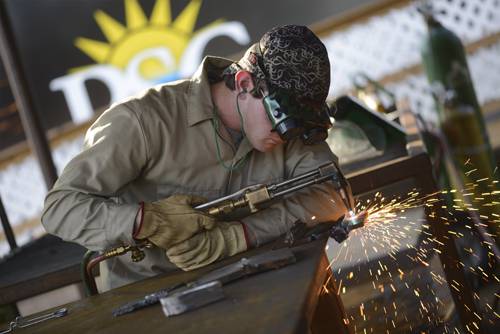 A student in welding gear welding metal with sparks flying during hands-on training at Pensacola Sta.