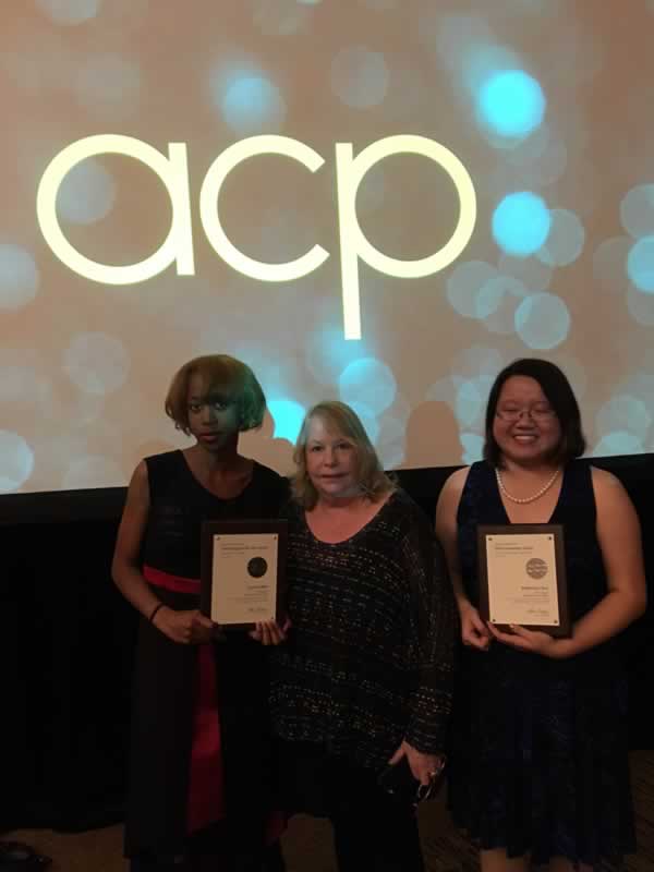 Three students holding awards at the National College Media Convention with the "acp" logo in the ba.