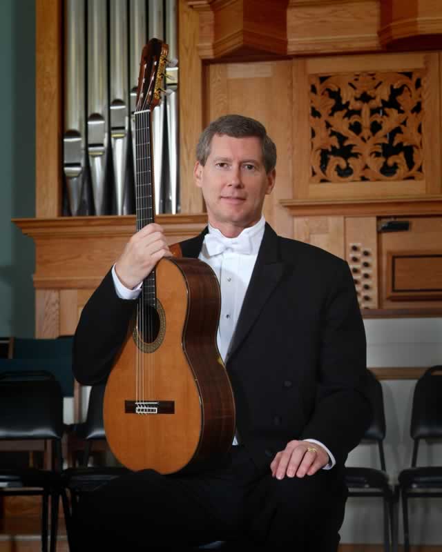 Highly skilled music professor holding classical guitar in a concert hall setting.