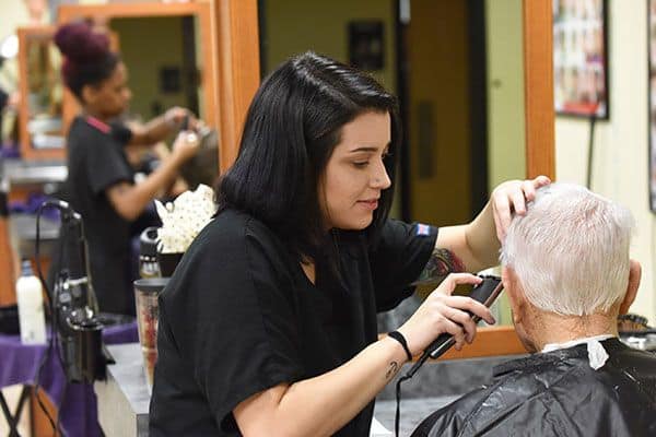 Hairdresser cutting elderly man's hair in a salon setting.