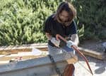 Lumberjack student using a saw on a wooden beam during hands-on learning.