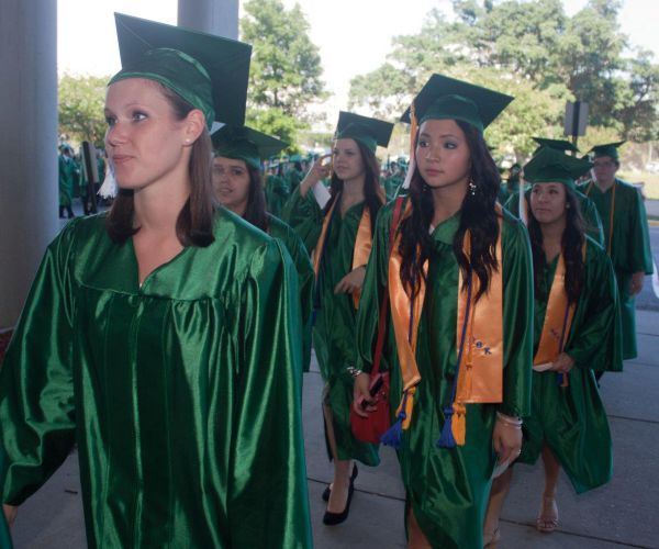 Group of diverse students in green caps and gowns at Pensacola State graduation.