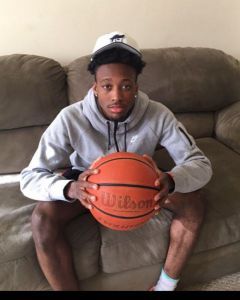 Young male college athlete holding basketball on sofa for sports team promotion.