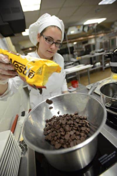 Culinary student pouring chocolate chips into a bowl in a professional kitchen.