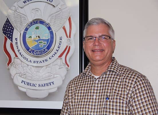 Campus safety officer at Pensacola State College standing near public safety emblem.