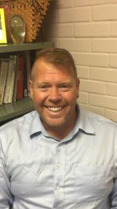Promoted PSC faculty member smiling in office.
