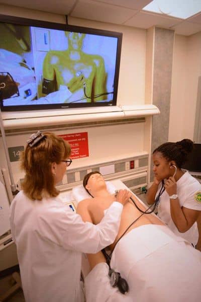 Nursing students practicing patient care on simulation mannequin for higher education training.