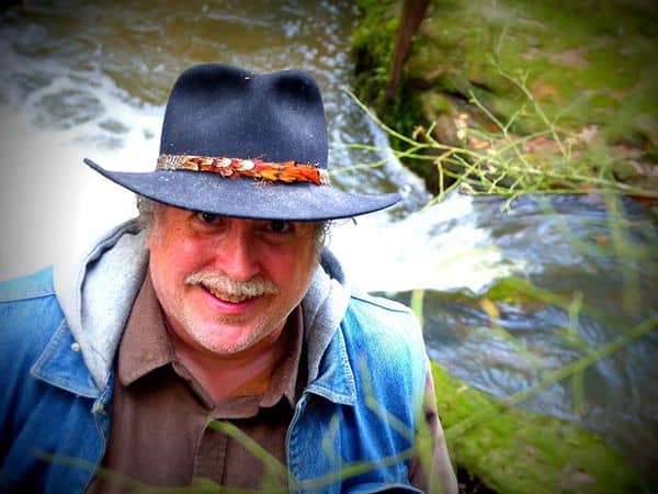 Vibrant outdoor scene with a smiling man wearing a hat near water at Pensacola State College.