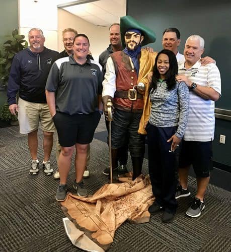 Group of diverse students and staff with pirate statue in classroom setting.