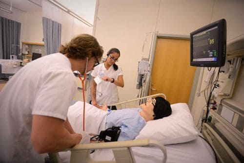 Medical students practicing patient care in a hospital simulation room.