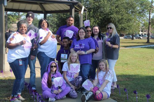 Group of diverse students and staff holding purple ribbons and butterfly signs for breast cancer awa.