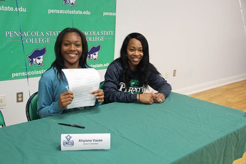 College students signing documents at a table with Pensacola State College branding in the backgroun.