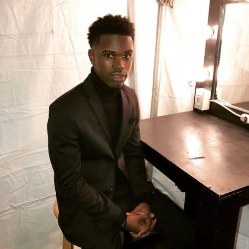 Young man in black suit sitting at a dressing table in backstage or dressing room.