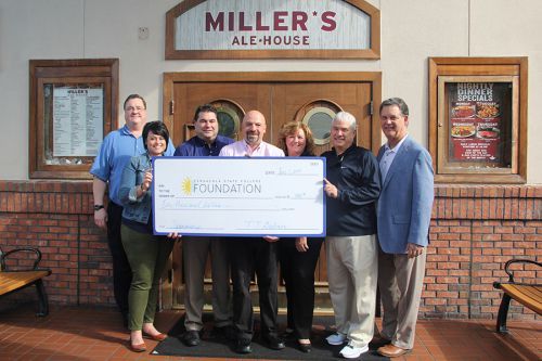 Group of diverse people holding a large donation check in front of Miller's Ale House.