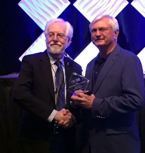 Two men in suits shaking hands at awards ceremony, celebrating welding program achievement.