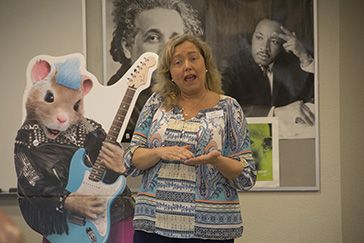 Engaging woman speaker at Pensacola State College event with mascot and portraits in background.