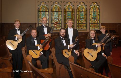 Classical guitar group performing in historic church with stained glass windows.