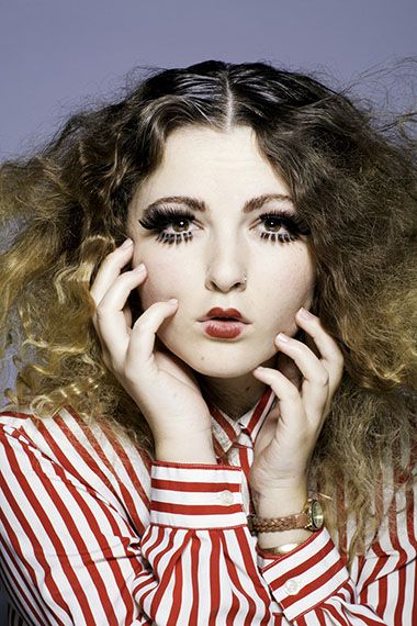 Woman with curly hair and makeup, wearing striped shirt, symbolizing resilience in education.