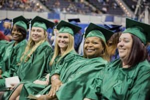 Students in green caps and gowns celebrating graduation at Pensacola State College.