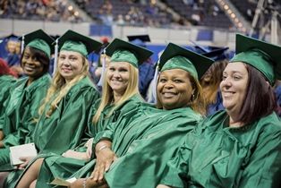 Students in green caps and gowns celebrating graduation at Pensacola State College.