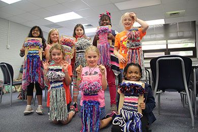 Children holding vibrant handmade craft projects in a classroom setting.