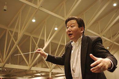 Conductor guiding an orchestra during a performance in a contemporary concert hall.