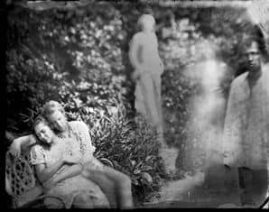 Black and white photo of two women sitting outdoors, with two ghostly figures in the background, par.