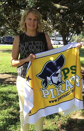 Woman holding Pensacola State College Pioneers flag outdoors under trees.