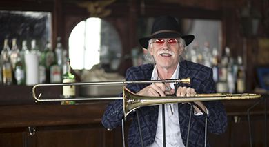 Jazz musician with a trombone at a bar, smiling and wearing a hat.