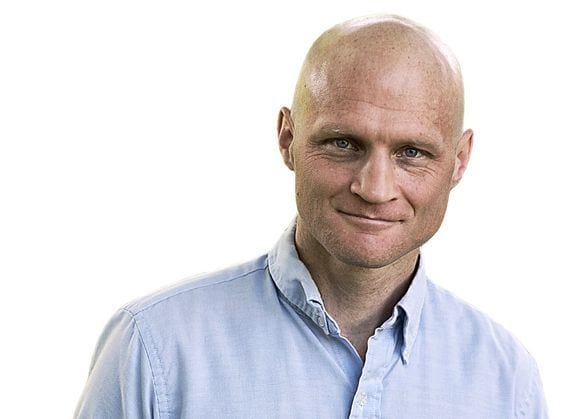 Bald man in a light blue shirt smiling at a public lecture event.