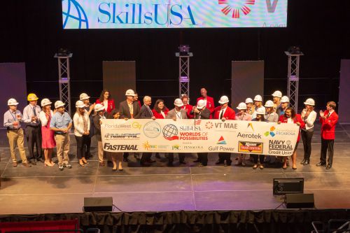 Students and instructors celebrate at SkillsUSA event on stage with banners.