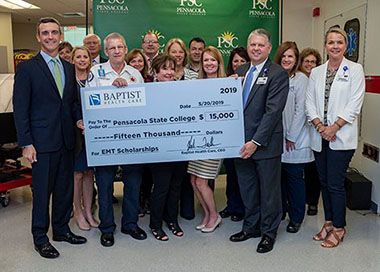 Group of students and officials holding a scholarship check for EMT students at Pensacola State Coll.