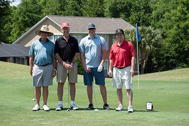 Group of four men posing on golf course after tournament.
