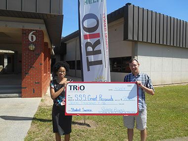 Two students holding a large TRIO&ndash;SSS grant check outside campus building.