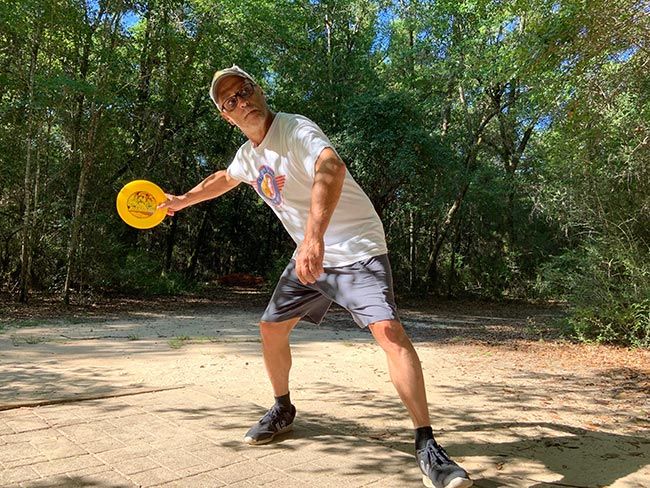 Disc golf player throwing disc on outdoor course at Pensacola State College.