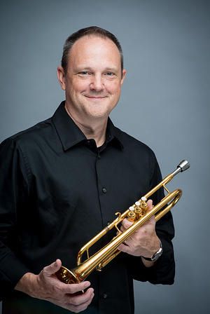 Music educator with trumpet, promoting Pensacola State College's music program.