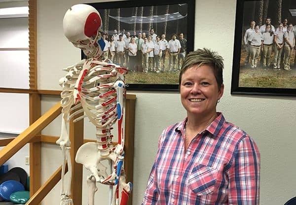Highly accessible image of a woman smiling next to a human skeleton model in an educational setting.