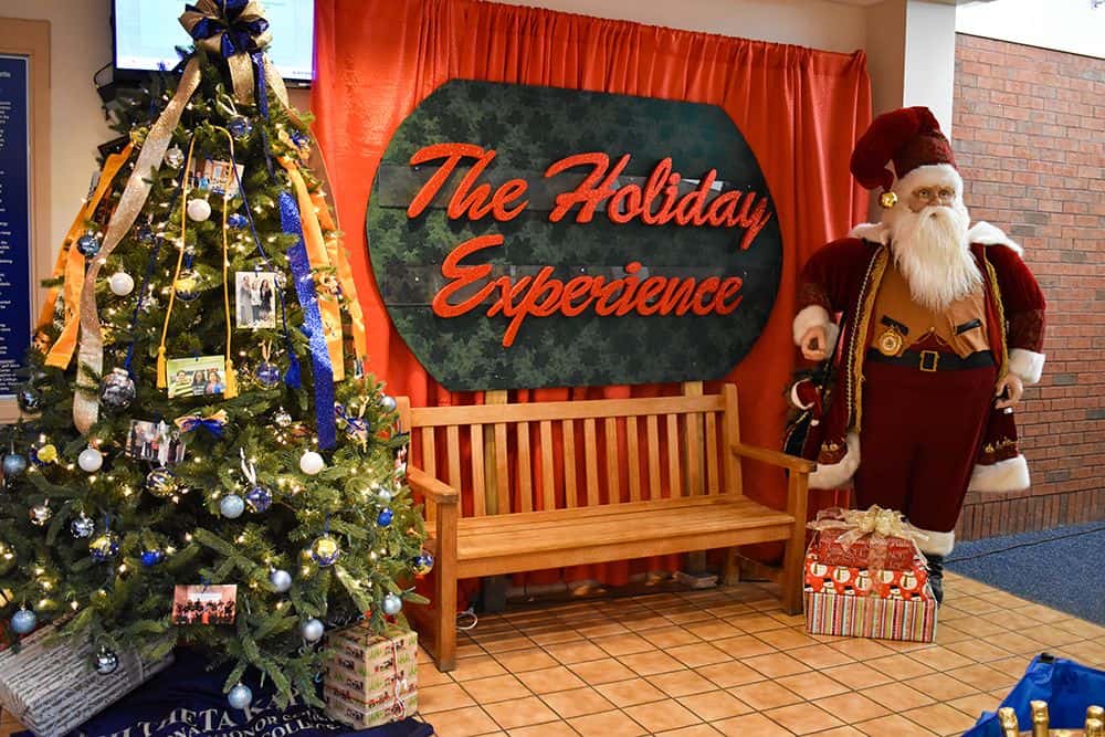 Festive holiday scene with decorated Christmas tree, Santa Claus figure, and scholarship fundraising.