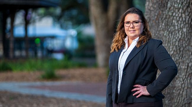 Female cybersecurity student in professional attire outdoors at Pensacola State College.