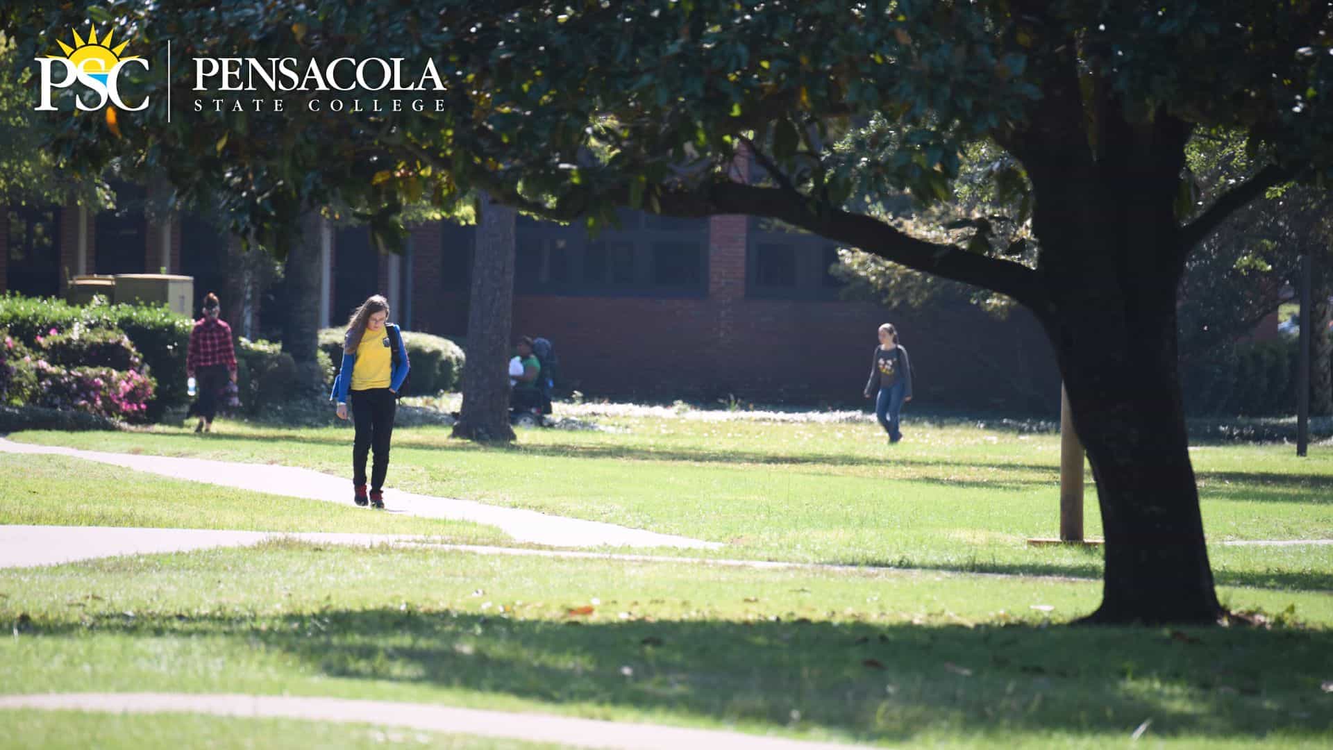 Students walking on college campus with lush greenery and large trees at Pensacola State College for.
