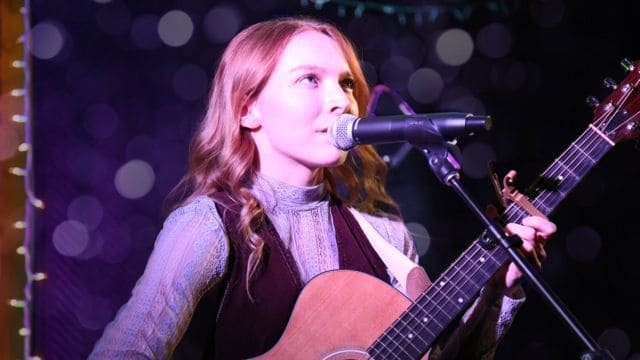 Talented Pensacola State alumna singing and playing guitar during a live music performance in Music.
